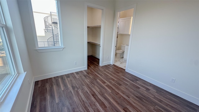 unfurnished bedroom with a walk in closet, connected bathroom, dark hardwood / wood-style flooring, and a closet