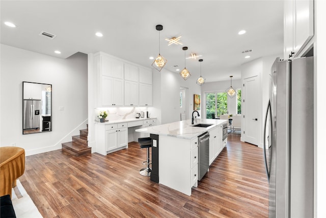 kitchen with appliances with stainless steel finishes, pendant lighting, an island with sink, sink, and white cabinets