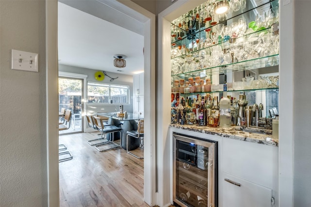 bar featuring white cabinets, light stone countertops, beverage cooler, and light hardwood / wood-style flooring