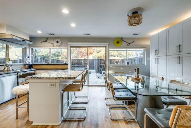 kitchen with a center island, a kitchen breakfast bar, light stone counters, range hood, and light hardwood / wood-style floors