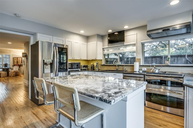 kitchen with white cabinetry, a wealth of natural light, stainless steel appliances, dark stone countertops, and a kitchen island