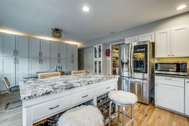 kitchen with backsplash, light stone countertops, light wood-type flooring, white cabinetry, and stainless steel appliances