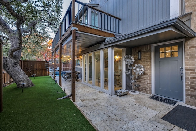 view of exterior entry featuring a balcony, a patio area, and a lawn