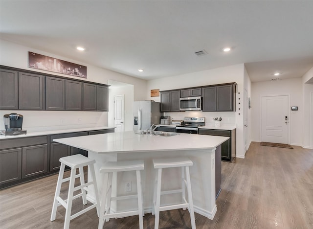 kitchen featuring sink, stainless steel appliances, a kitchen island with sink, dark brown cabinets, and light wood-type flooring