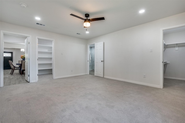 unfurnished bedroom featuring ceiling fan, a walk in closet, and light carpet