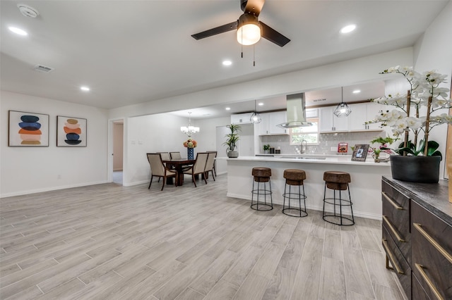 kitchen with a kitchen breakfast bar, island range hood, white cabinets, light hardwood / wood-style floors, and hanging light fixtures