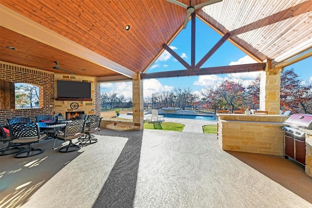 view of patio / terrace with an outdoor stone fireplace, ceiling fan, and exterior kitchen