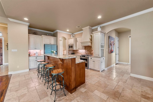 kitchen featuring a center island with sink, appliances with stainless steel finishes, tasteful backsplash, light stone counters, and a breakfast bar area