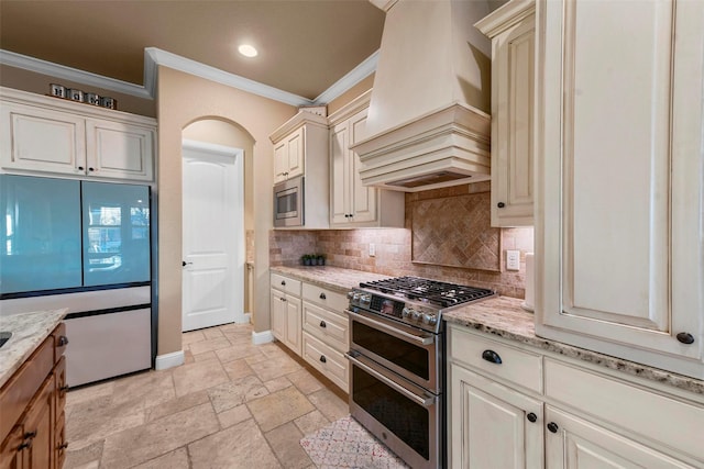 kitchen with light stone countertops, ornamental molding, premium range hood, and stainless steel appliances