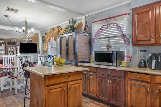 kitchen with dark wood-type flooring, crown molding, pendant lighting, a chandelier, and a kitchen island