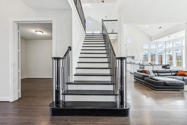 staircase featuring high vaulted ceiling, sink, hardwood / wood-style floors, and a notable chandelier