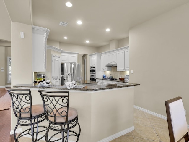 kitchen with a breakfast bar, appliances with stainless steel finishes, kitchen peninsula, dark stone counters, and white cabinets