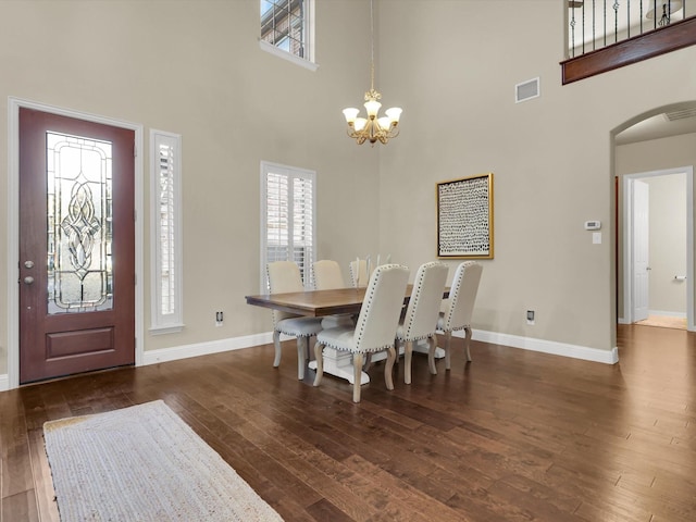 dining space with dark wood-type flooring, a towering ceiling, and a chandelier