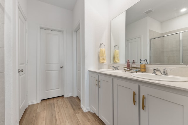 bathroom featuring tiled shower, wood finished floors, visible vents, and a sink