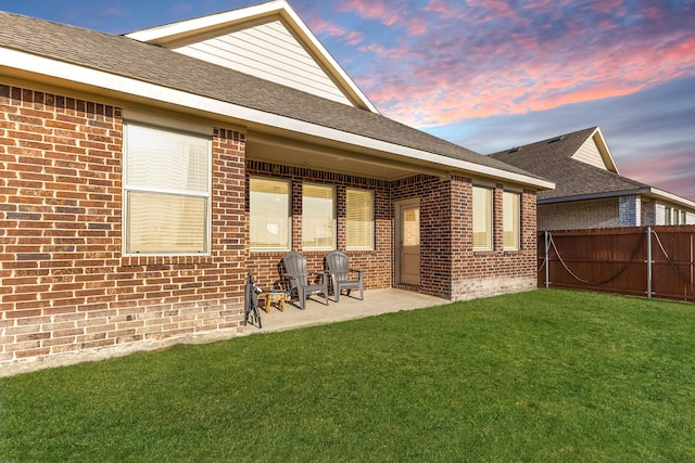 rear view of property featuring brick siding, a patio, fence, and a lawn