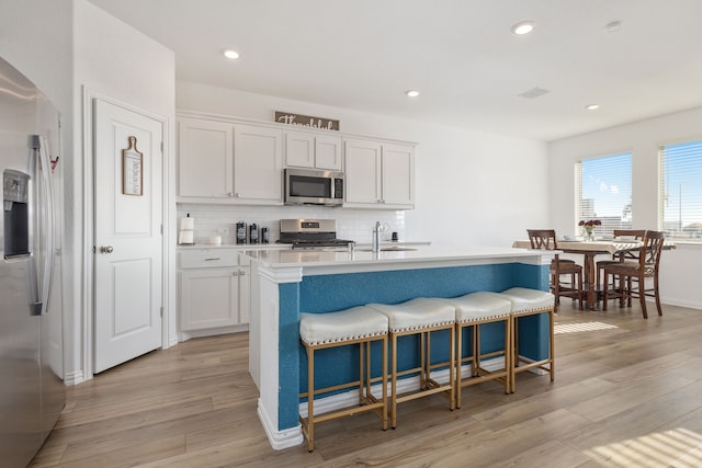 kitchen with a breakfast bar area, light wood finished floors, white cabinets, appliances with stainless steel finishes, and backsplash