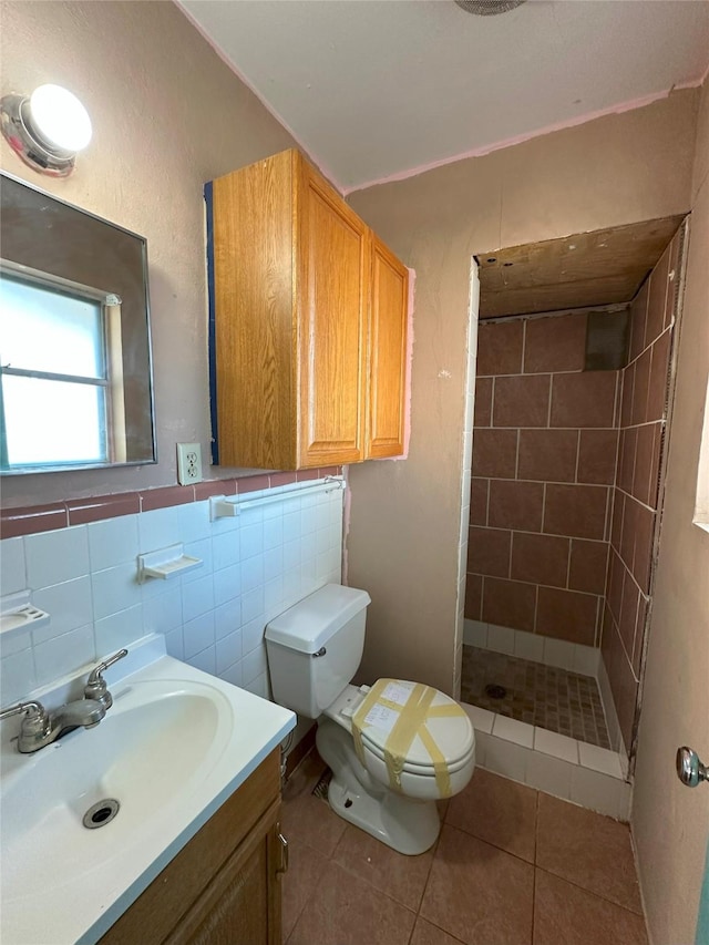 bathroom with tile patterned floors, vanity, tiled shower, tile walls, and toilet