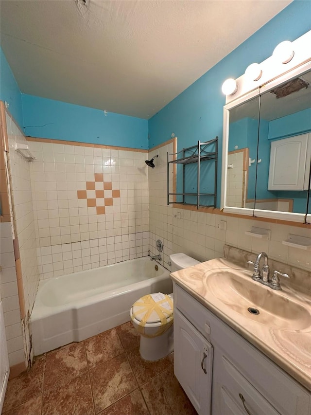 full bathroom with tile walls, vanity, a textured ceiling, tiled shower / bath, and toilet