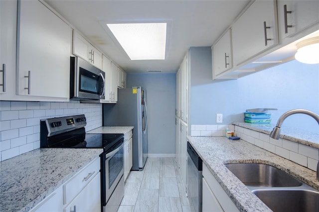 kitchen featuring a skylight, light stone counters, stainless steel appliances, sink, and white cabinets