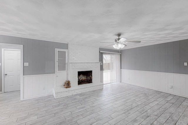 unfurnished living room with a fireplace, ceiling fan, and light wood-type flooring