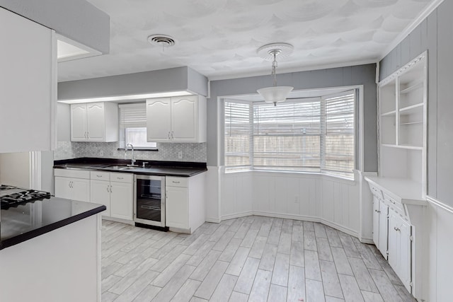 kitchen with sink, decorative light fixtures, beverage cooler, light hardwood / wood-style floors, and white cabinets