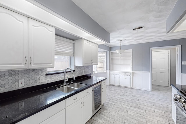 kitchen with stainless steel stove, decorative light fixtures, sink, wine cooler, and white cabinets