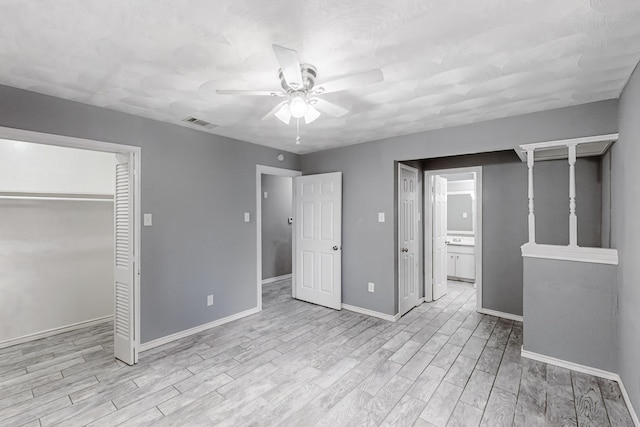 unfurnished bedroom featuring ceiling fan, a closet, ensuite bath, and light wood-type flooring