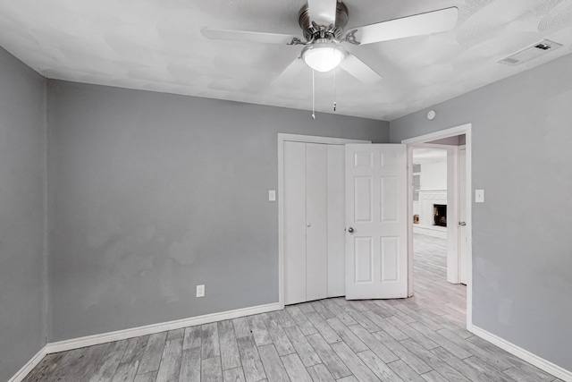 unfurnished bedroom with ceiling fan, a brick fireplace, light wood-type flooring, and a closet