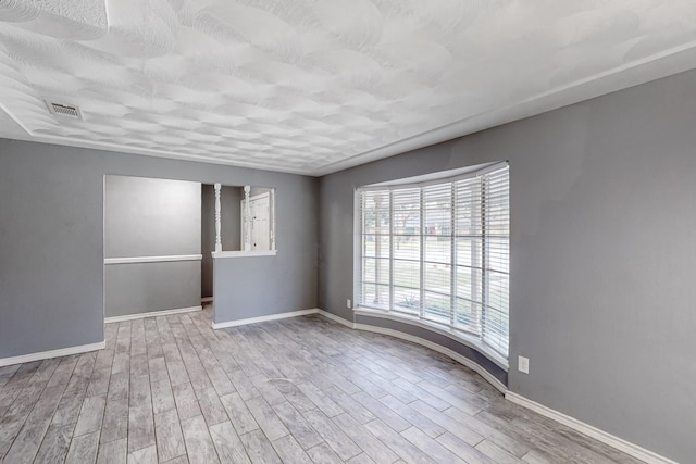 unfurnished room featuring a textured ceiling and light hardwood / wood-style flooring