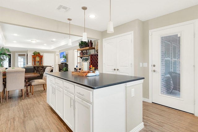 kitchen with light wood-type flooring, a raised ceiling, white cabinets, a center island, and hanging light fixtures