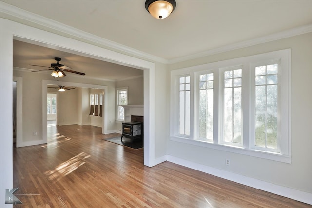 unfurnished living room with wood-type flooring, a wood stove, ornamental molding, and a healthy amount of sunlight