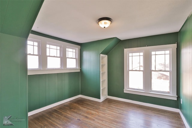 bonus room with dark wood-type flooring and wood walls