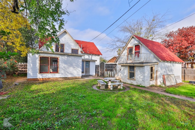 rear view of property featuring a balcony and a yard