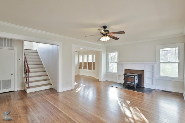 unfurnished living room with wood-type flooring, a wood stove, ceiling fan, and crown molding