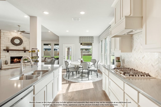 kitchen featuring sink, dishwasher, a fireplace, white cabinets, and stainless steel gas stovetop