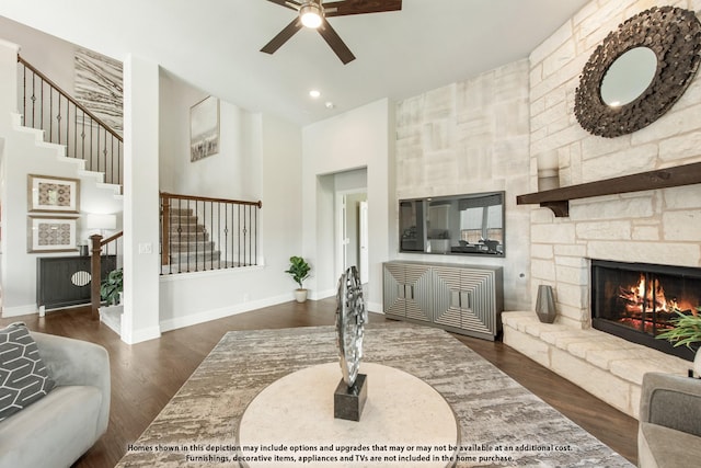 living room with ceiling fan, dark wood-type flooring, a fireplace, and a towering ceiling