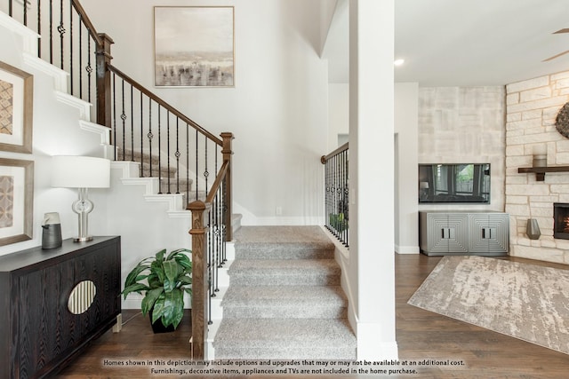 stairs with wood-type flooring, a stone fireplace, and a high ceiling