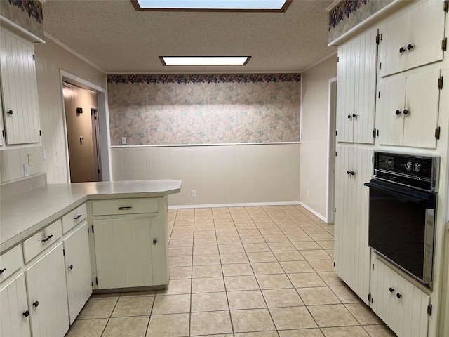 kitchen featuring black oven, white cabinets, light tile patterned flooring, and a textured ceiling