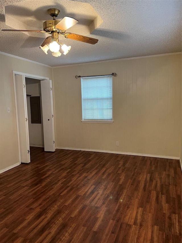 empty room with ceiling fan, dark hardwood / wood-style floors, wood walls, a textured ceiling, and ornamental molding