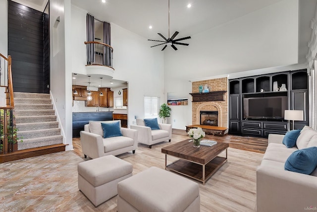 living room with ceiling fan, light wood-type flooring, high vaulted ceiling, and a brick fireplace