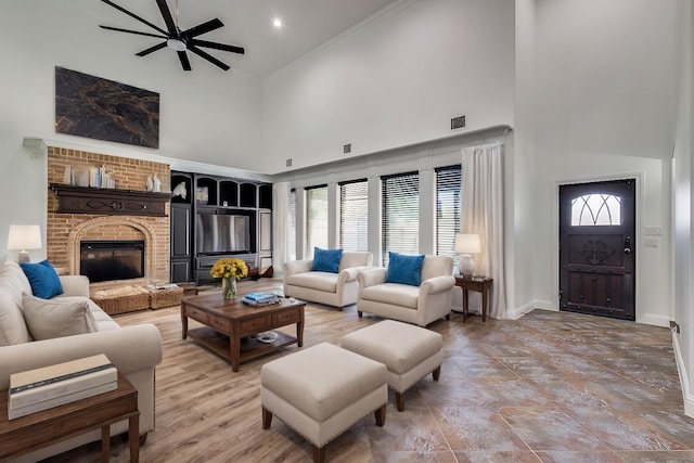 living room with ceiling fan, a towering ceiling, and a brick fireplace