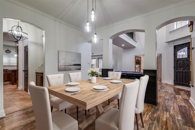 dining space with a towering ceiling, dark hardwood / wood-style flooring, crown molding, and a notable chandelier