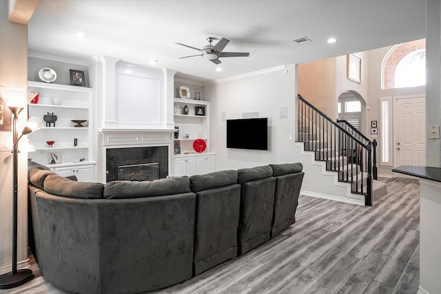 living room featuring ceiling fan, light wood-type flooring, crown molding, and a tiled fireplace