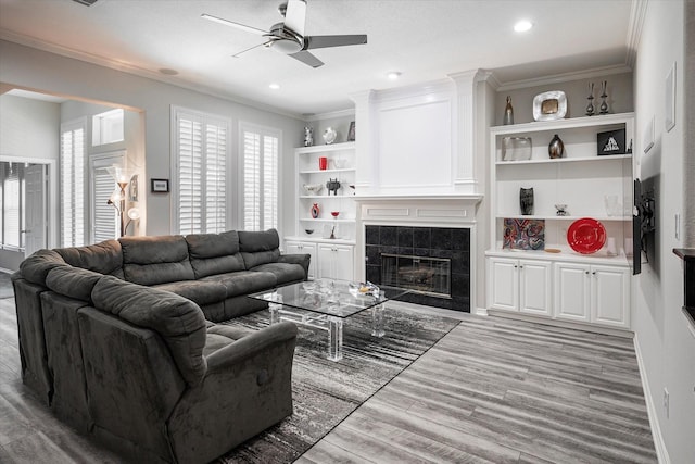 living room featuring ceiling fan, ornamental molding, a tile fireplace, and light hardwood / wood-style flooring