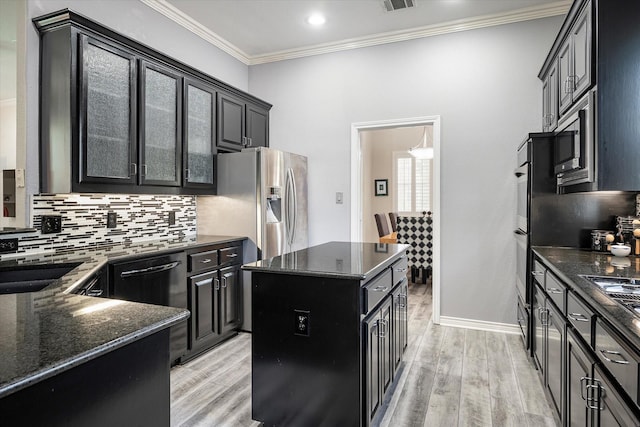 kitchen with a center island, crown molding, light hardwood / wood-style flooring, dark stone countertops, and stainless steel appliances