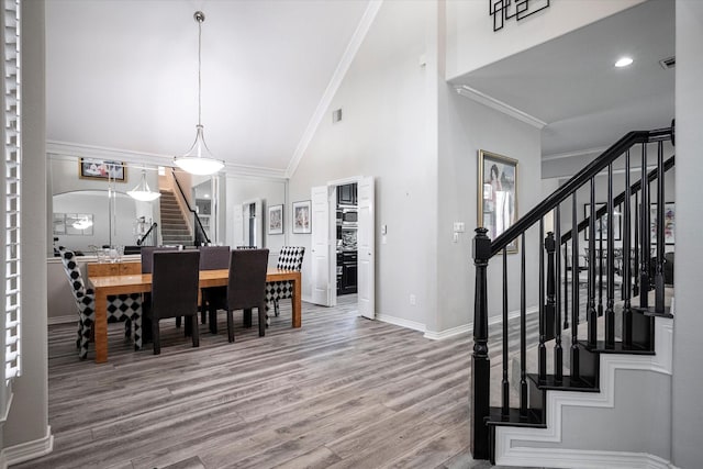 dining area featuring wood-type flooring, crown molding, and high vaulted ceiling