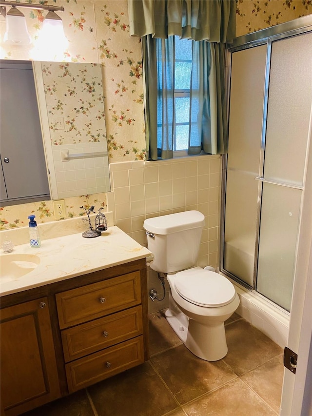 bathroom featuring tile patterned floors, vanity, a shower with door, tile walls, and toilet