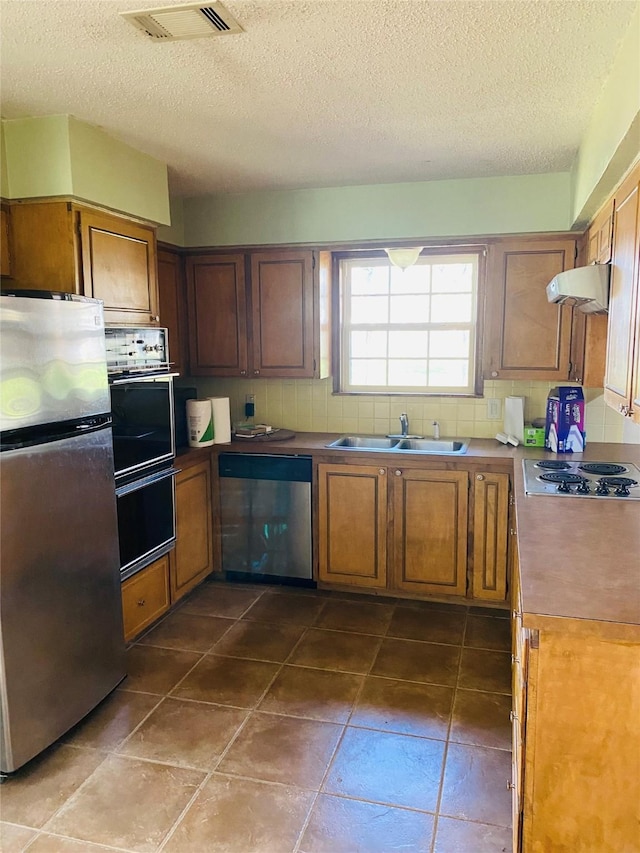 kitchen with appliances with stainless steel finishes, backsplash, extractor fan, dark tile patterned floors, and sink