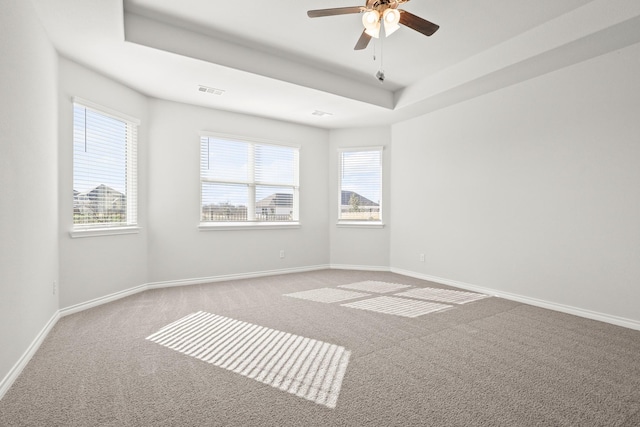 empty room featuring a tray ceiling, plenty of natural light, light colored carpet, and ceiling fan