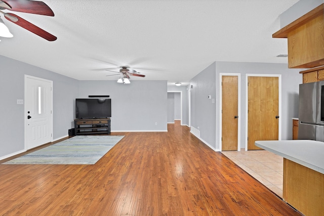 unfurnished living room with ceiling fan, a textured ceiling, and light hardwood / wood-style flooring